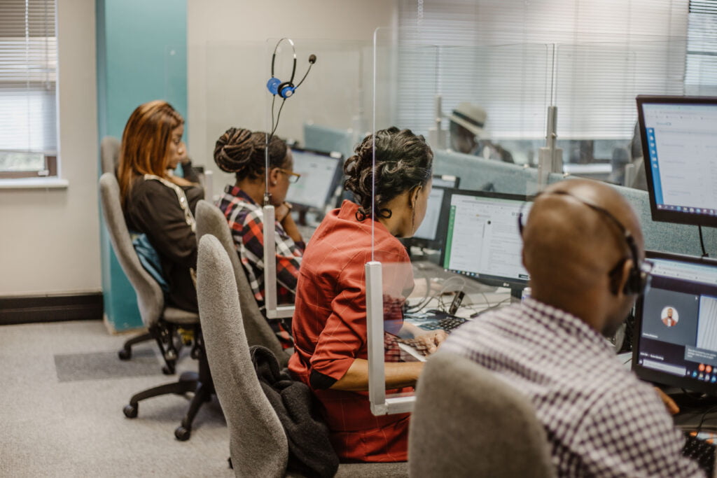 Agents in Zuid-Afrika zitten aan hun bureau en doen callcenter werk.